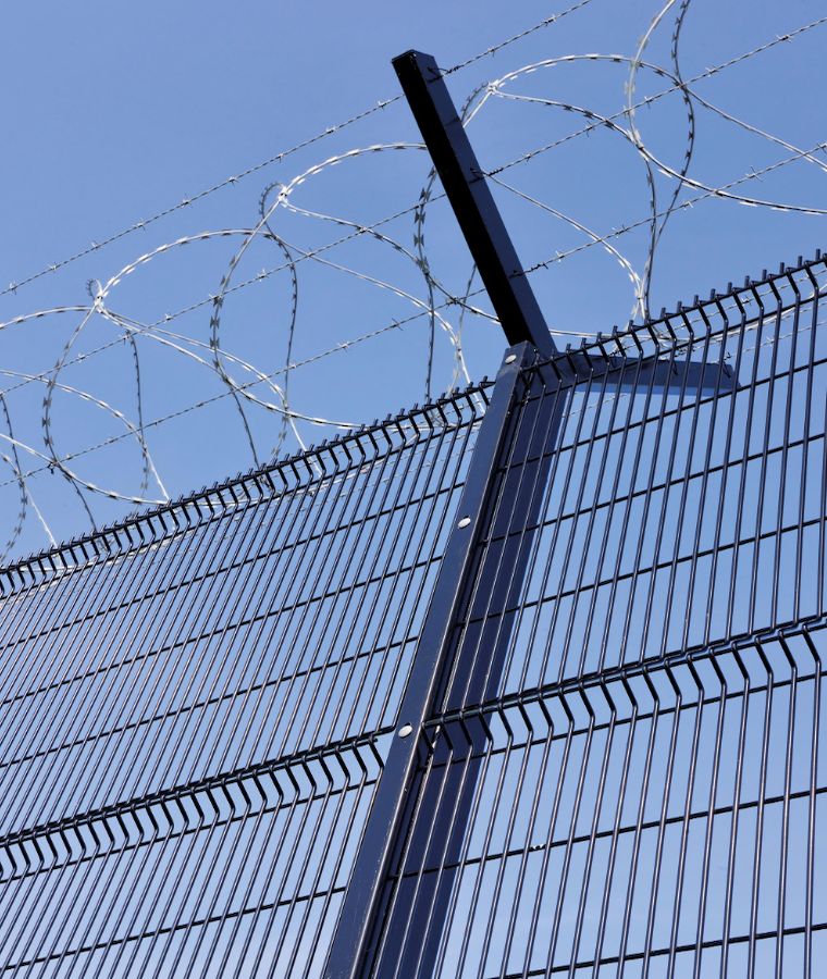 High-security 358 anti-climb mesh fence topped with razor coil against a blue sky.