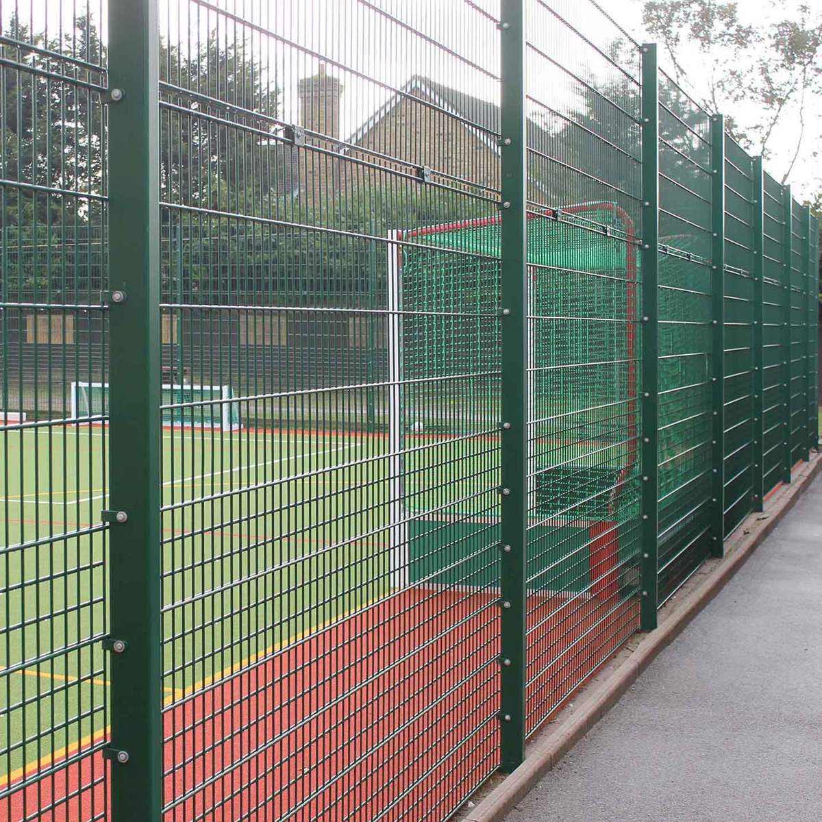 Green welded mesh sports fencing enclosing athletic courts at a school campus.