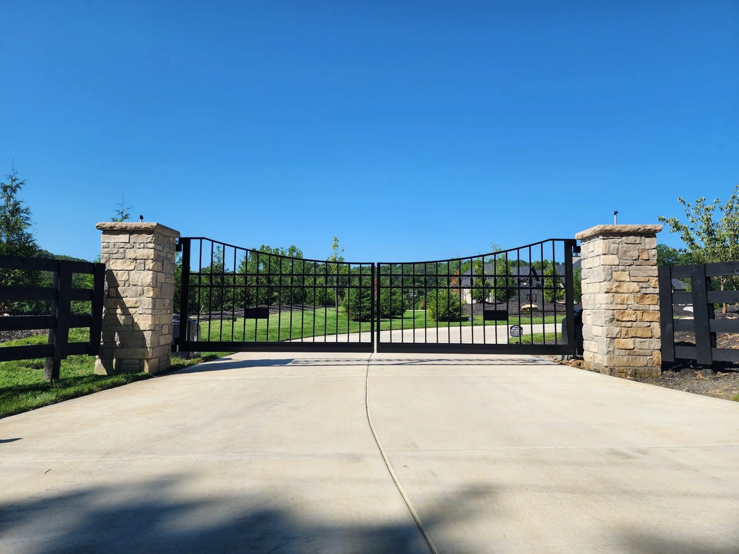 Dual-leaf ornamental steel entry gate with stone columns at a gated community.